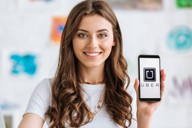 Kiev, Ukrayna - 17 Nisan 2019: Ekranda Uber uygulaması ile akıllı telefon sunan ve kameraya bakan güzel gülümseyen kız.