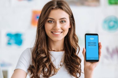 Kiev, Ukrayna - 17 Nisan 2019: Ekranda Skype uygulaması olan akıllı telefonu gösteren ve kameraya bakan mutlu gülümseyen kız.