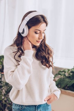 pensive genç kız kulaklık müzik dinleme, cebinde el tutarak ve aşağı bakarak