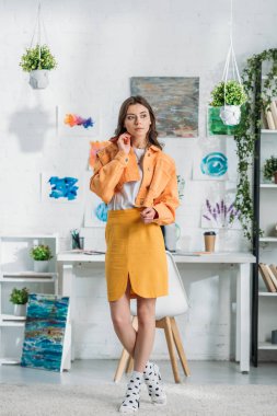 duvarda yeşil bitkiler ve resimlerle dekore edilmiş geniş bir odada dururken uzaklara bakan çekici trendy kız