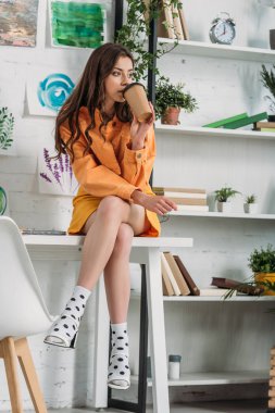 raf yakınında masada otururken tek kullanımlık fincandan kahve içen düşünceli kız