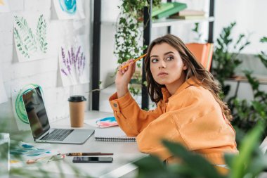 düşünceli genç kadın dizüstü bilgisayar yakınında masada oturan ve uzağa bakarak seçici odak 