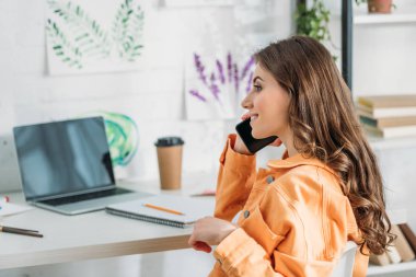 evde masa başında dizüstü otururken akıllı telefonda konuşurken gülümseyen kız