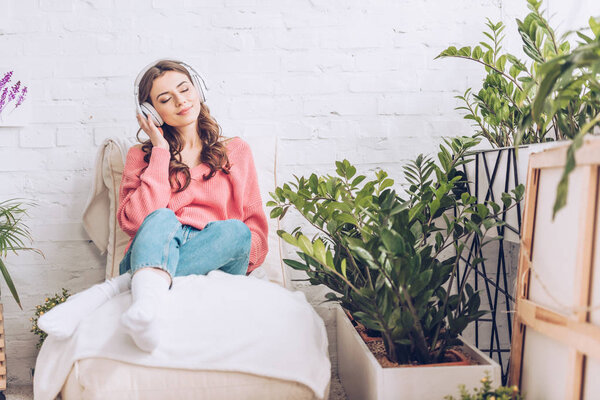 красивая девушка с закрытыми глазами расслабляется, сидя в мягком шезлонге и слушая музыку в наушниках
