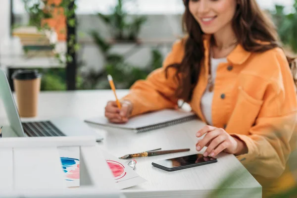 Partial View Smiling Girl Sitting Desk Using Smartphone Writing Notebook Royalty Free Stock Images