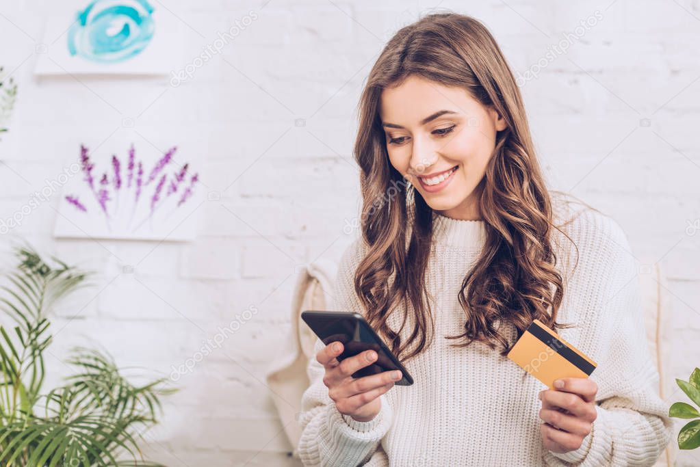 beautiful young woman smiling while holding credit card and using smartphone