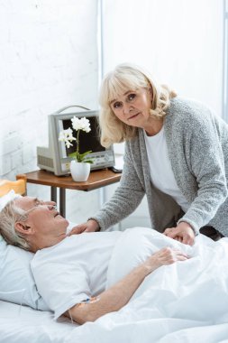 sad senior woman with husband in coma in hospital clipart