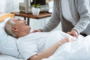 cropped view of senior woman with husband in coma in hospital clipart