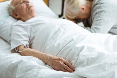 selective focus of sad senior woman with husband in coma in clinic clipart