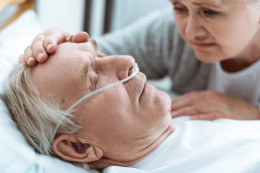 cropped view of senior woman with husband in coma in hospital clipart