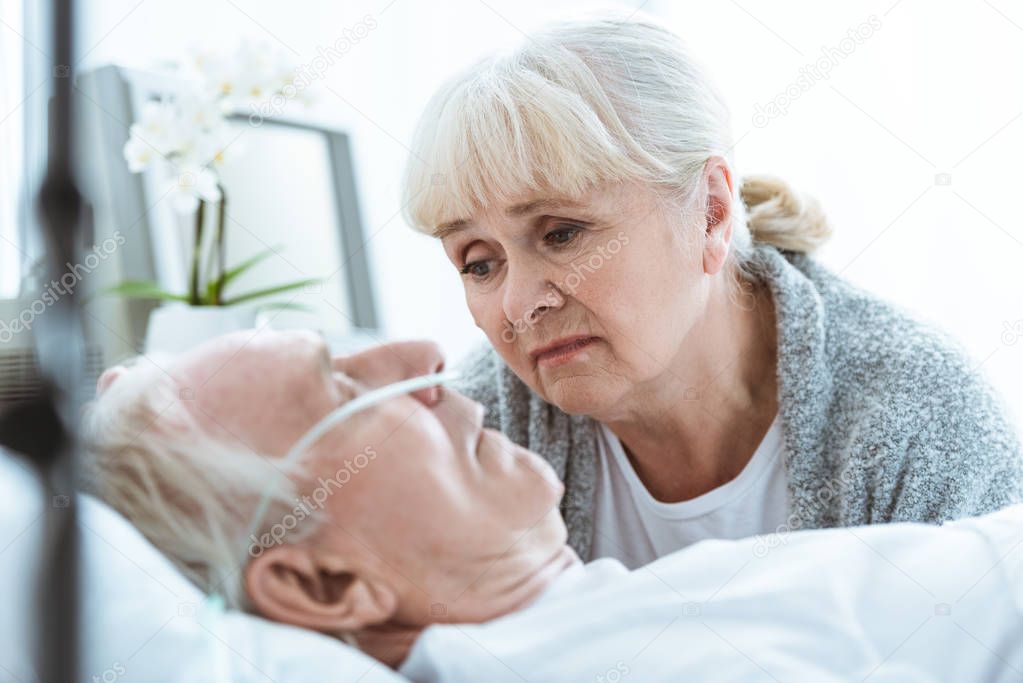 sad senior woman looking at husband in coma in clinic