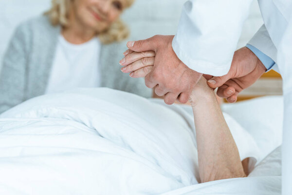 partial view of doctor standing near patient and checking pulse