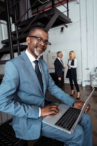 オフィスのパートナーの近くにラップトップを使用して幸せなアフリカ系アメリカ人の男性の選択的な焦点 — ストック写真