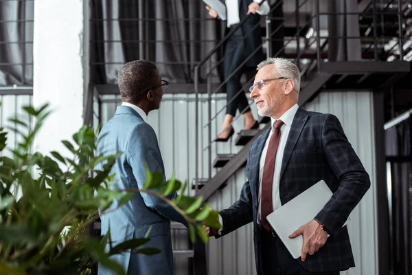 low angle view of businessman shaking hands with african american partner