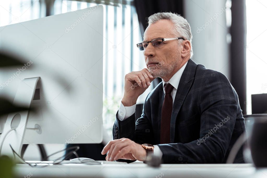 selective focus of businessman in glasses looking at computer monitor 