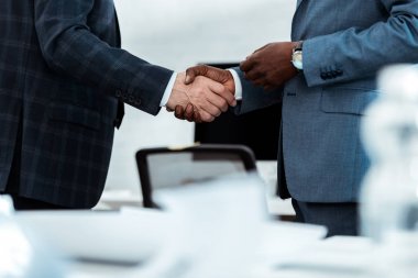 cropped view of african american businessman shaking hands with partner in office  clipart