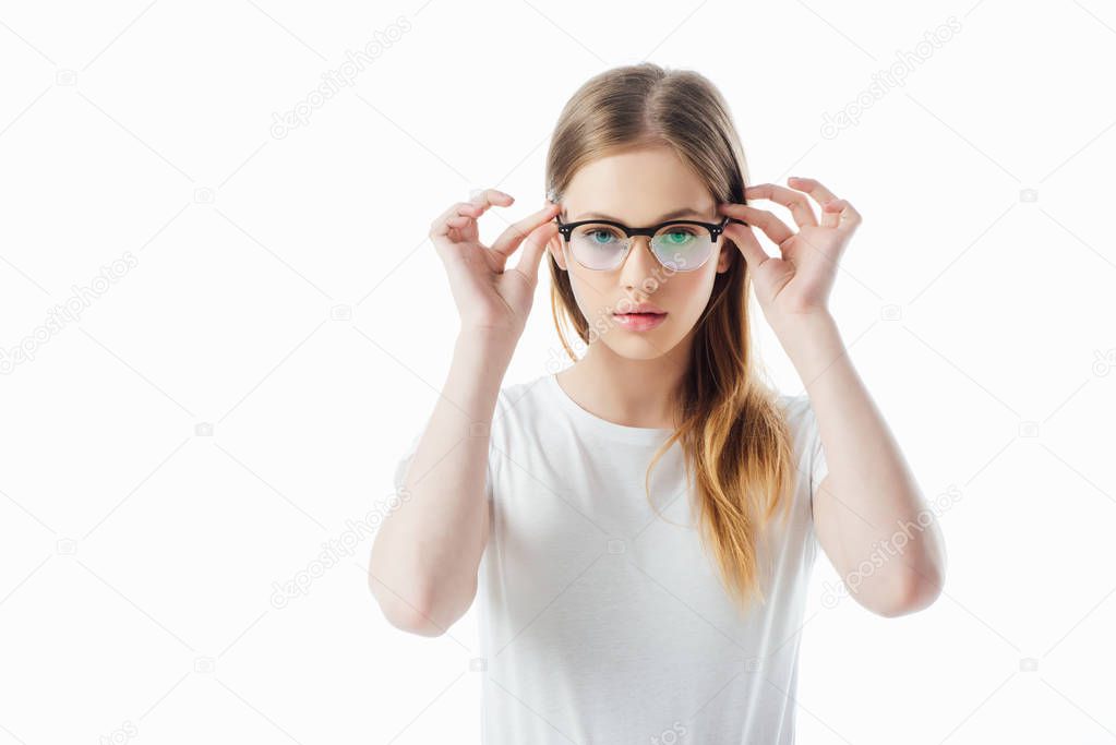 serious teenage girl touching glasses and looking at camera isolated on white