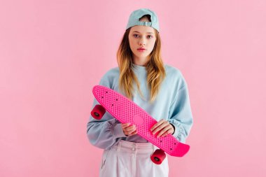 şapka tutan güzel genç kız pembe üzerinde izole Penny Board