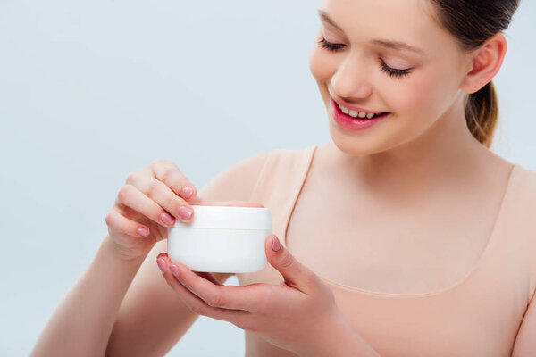 happy teenage girl holding cosmetic cream isolated on grey