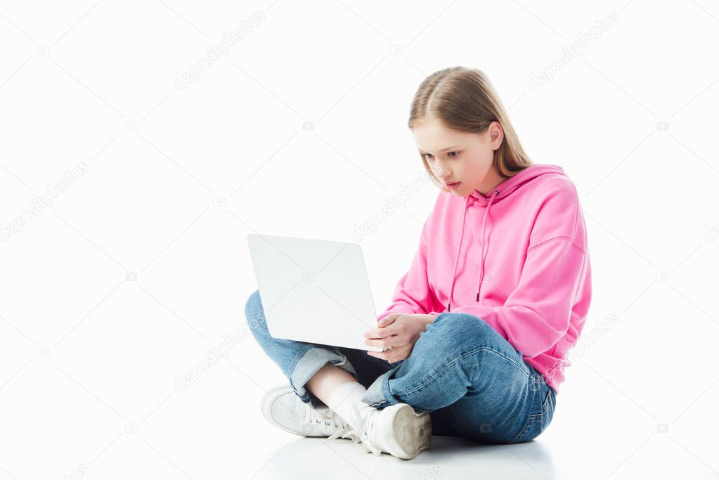 upset teenage girl with crossed legs using laptop isolated on white, illustrative editorial