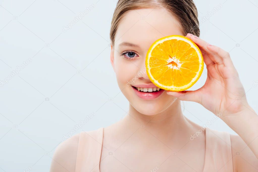 teenage girl with smile holding ripe orange half near face isolated on grey