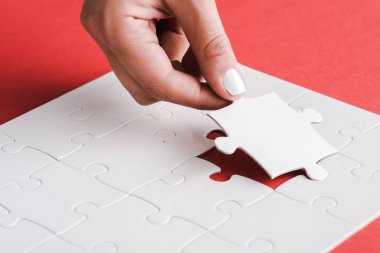 cropped view of woman holding white jigsaw near connected puzzle pieces on red clipart