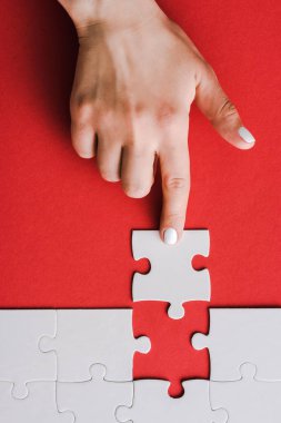 top view of woman pointing with finger at jigsaw near connected white puzzle pieces on red clipart