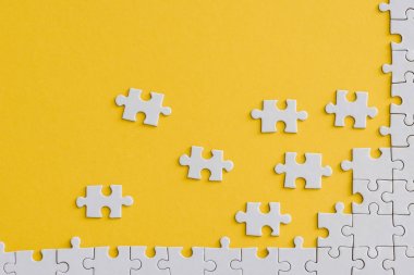 top view of unfinished jigsaw near connected white puzzle pieces isolated on yellow  clipart
