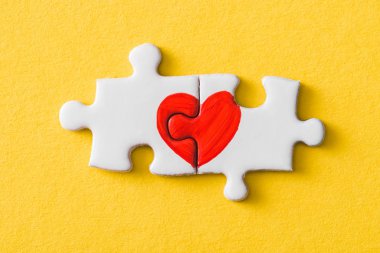 top view of connected puzzle pieces with drawn red heart isolated on yellow  clipart