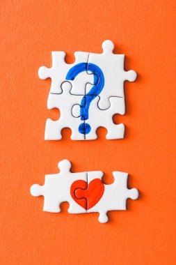 top view of connected puzzle pieces with drawn red heart and blue question mark on orange clipart