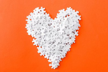 top view of heart-shaped jigsaw puzzle pieces isolated on orange clipart