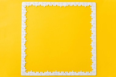 top view of frame with connected white jigsaw puzzle pieces isolated on yellow  clipart
