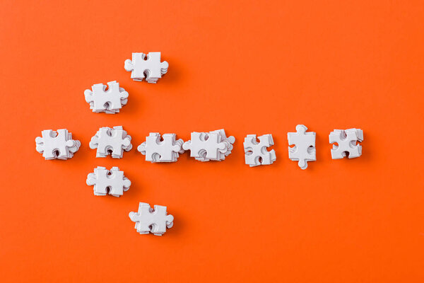 top view of white direction arrow with jigsaw puzzle pieces on orange