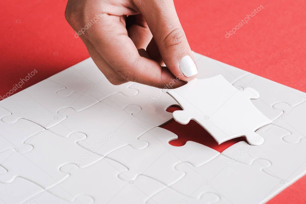 cropped view of woman holding white jigsaw near connected puzzle pieces on red