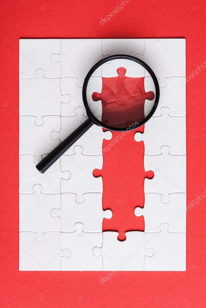 top view of magnifying glass near white puzzle pieces on red 