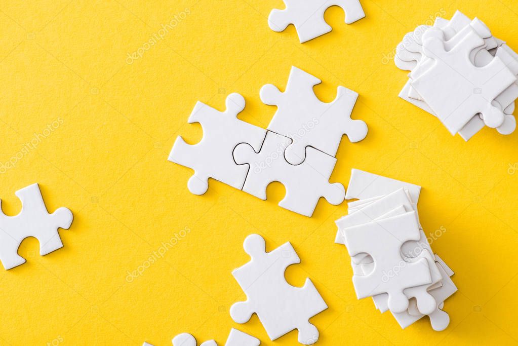top view of white stack of jigsaw near connected puzzles isolated on yellow 