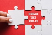 top view of woman touching jigsaw near break the rules lettering and connected white puzzle pieces and idea lettering on red