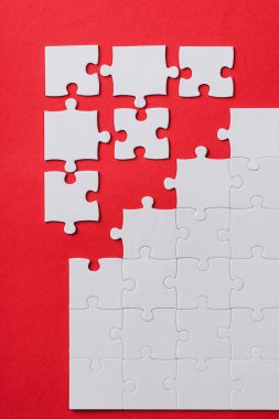 top view of white connected and separate jigsaw puzzle pieces isolated on red  clipart