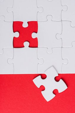 top view of incomplete white puzzles near separate piece isolated on red  clipart
