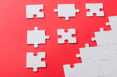 white connected and separate jigsaw puzzle pieces isolated on red  clipart