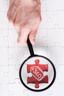 beyaz bağlı bulmaca parçaları yakın seo yazı ile yapboz yakınında büyüteç tutan adam üst görünümü 