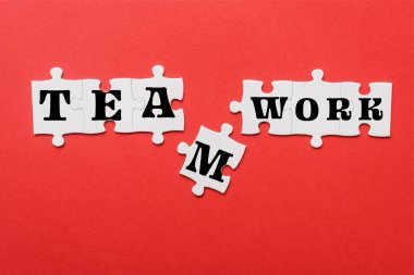 top view of white connected jigsaw near puzzle piece with teamwork lettering isolated on red  clipart