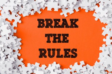 top view of frame of white jigsaw puzzle pieces around break the rules lettering on orange clipart