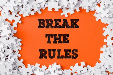 top view of frame of white jigsaw puzzle pieces around break the rules lettering on orange clipart