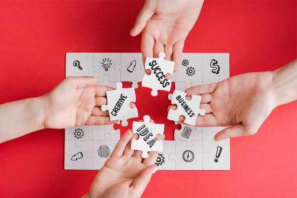 top view of man and woman holding white puzzle pieces with creative, idea, business and success words on white 