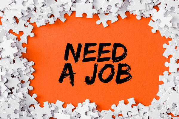 top view of frame of white jigsaw puzzle pieces around of need a job lettering on orange