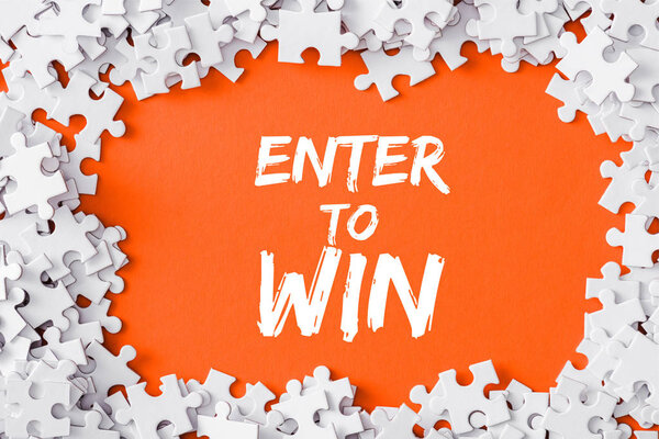 top view of frame of white jigsaw puzzle pieces around of enter to win lettering on orange