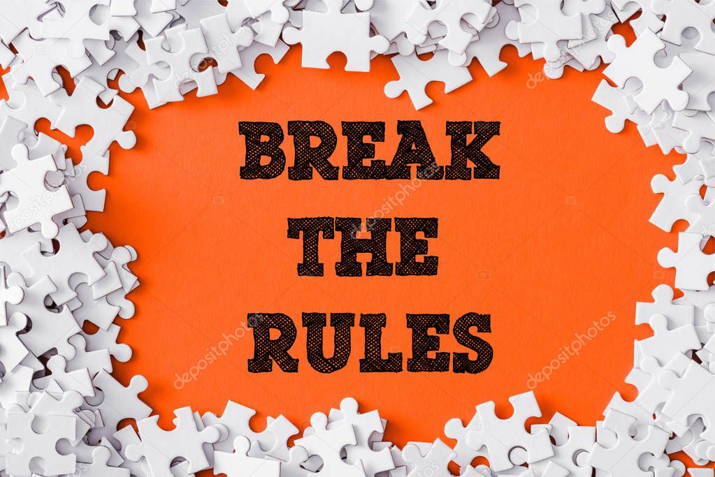 top view of frame of white jigsaw puzzle pieces around break the rules lettering on orange