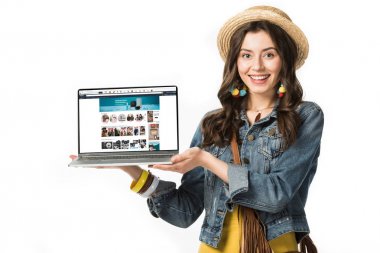 KYIV, UKRAINE - FEBRUARY 4, 2019: smiling hippie girl in straw hat holding laptop with amazon website on screen isolated on white clipart