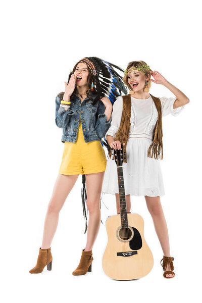 full length view of two bisexual hippie girls in indian headdress and wreath with acoustic guitar isolated on white